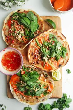 three pita breads on a cutting board topped with fresh vegetables and salsa sauce