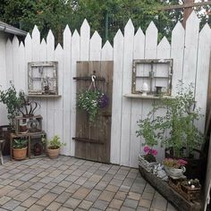 an outdoor garden with potted plants and wooden doors on the side of a white fence