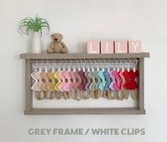 there is a shelf with clothes and a teddy bear on it that says grey frame / white clips