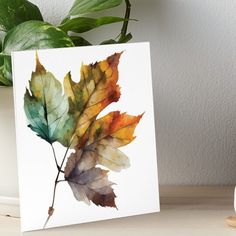 a watercolor painting of an autumn leaf art board print