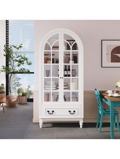 a white china cabinet sitting next to a dining room table with blue chairs and a potted plant