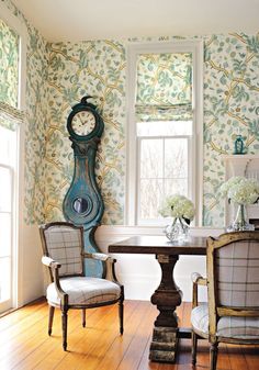 two chairs and a table in front of a window with a clock on the wall