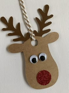 a reindeer ornament hanging from a string on a white wall with red glitter eyes