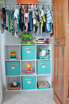 an organized closet with baby's clothes hanging on the rack and toy bins