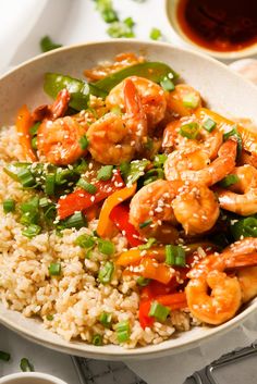 a white bowl filled with rice and shrimp on top of a table next to sauce