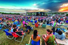 a crowd of people sitting in lawn chairs on top of a grass covered field at sunset