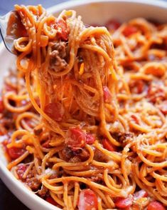 a spoon full of spaghetti with meat and tomato sauce on it, being lifted from a bowl