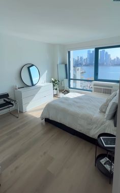 a bedroom with a bed, dresser and large window overlooking the cityscape is shown