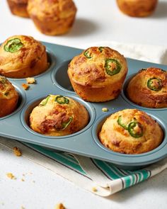 several muffins in a blue tray with green peppers on top and other muffins behind them