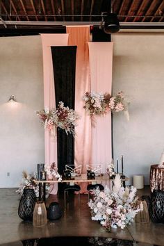 a table topped with lots of flowers next to two black vases filled with white and pink flowers