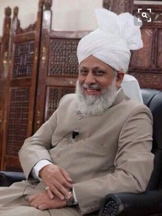 a man with a white turban sitting in a chair and smiling at the camera