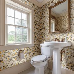 a white toilet sitting next to a sink in a bathroom under a window with yellow flowers on it