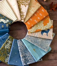 an assortment of fabric samples arranged in a circle on a wooden table with autumn leaves