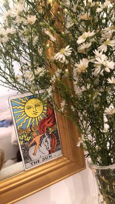 a vase filled with white flowers next to a framed tarot card on a table