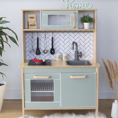 a toy kitchen with green cabinets and white tile backsplash, potted plants on the counter