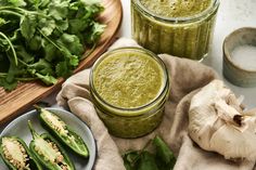 two jars filled with pesto sauce next to green vegetables