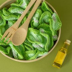 a bowl filled with green crocheted leaves next to a bottle of olive oil