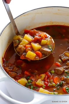 a ladle full of stew being held by a person with a spoon in it