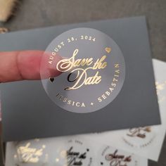 a person holding up a sticker that says save the date with gold lettering on it