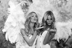 two beautiful women dressed in white posing for the camera with feathers on their shoulders and arms