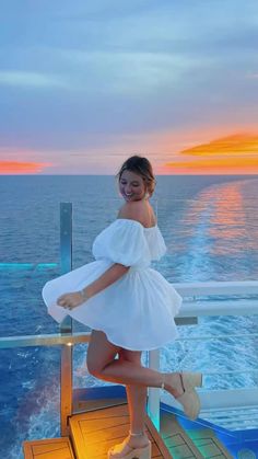 a woman standing on the deck of a cruise ship at sunset with her legs in the air