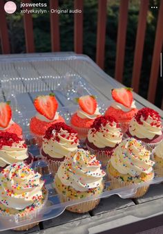 cupcakes with strawberries and sprinkles on them are sitting in plastic containers