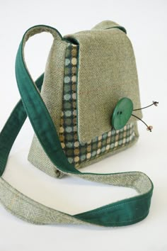 a small purse with a green button on the side and a long strap around it