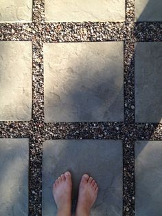 a person's bare feet standing on a tile floor with pebbles in the background