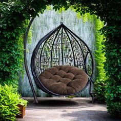 a hanging chair in the shape of a birdcage surrounded by greenery and potted plants