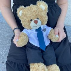 a woman holding a brown teddy bear wearing a dress and tie with her hands on her hips