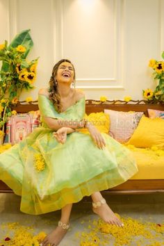 a woman in a green dress sitting on a bed with yellow flowers all around her