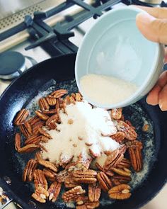 someone is adding sugar to some pecans in a skillet