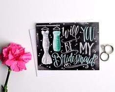 there is a card that says will you be my bridesmaid? and a pink carnation next to it