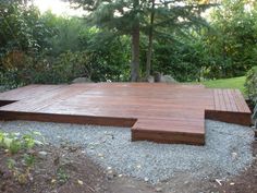 a wooden deck surrounded by gravel and trees