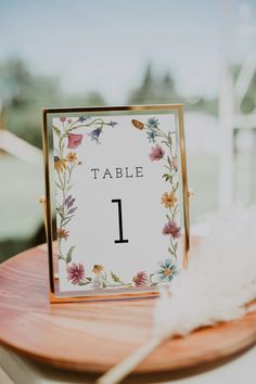 a table number is placed on top of a wooden board with flowers and feathers around it