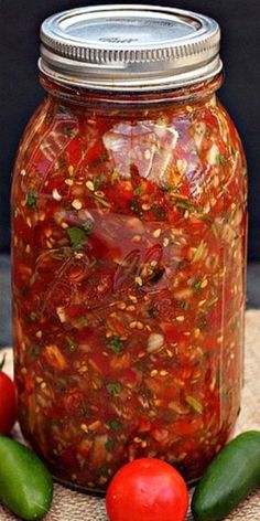 a jar filled with pickles and sauce on top of a table next to tomatoes