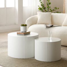 two white coffee tables sitting on top of a rug in front of a couch and window