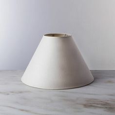 a white lamp shade sitting on top of a table next to a vase with flowers in it