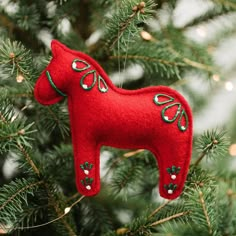 a red felt horse ornament hanging from a christmas tree with lights in the background