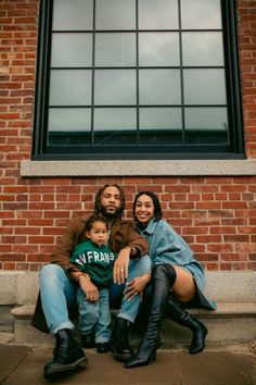 a man, woman and child sitting on the ground in front of a brick building