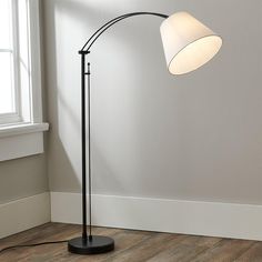 a black floor lamp with a white shade on it in an empty room next to a window