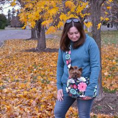 a woman is standing in the leaves with her small dog, wearing a floral purse