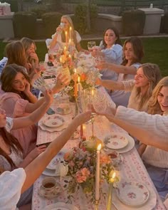 a group of women sitting around a table with plates and glasses on it, all holding candles