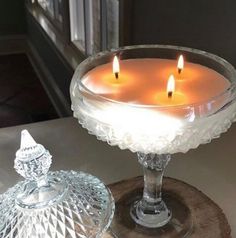 three lit candles sit in a glass bowl on a wooden stand next to a window