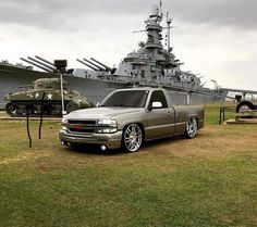 a silver truck parked in front of a large ship with tanks on the back ground