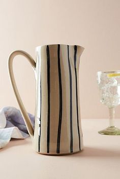 a white and black striped pitcher sitting next to a wine glass on a pink surface