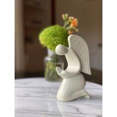 a white angel figurine sitting on top of a table next to a vase with flowers