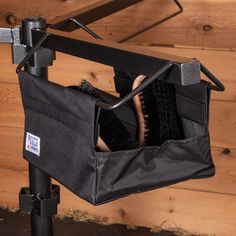 a brush and comb in a black bag hanging on a wooden wall next to a pair of scissors