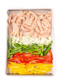 assorted sliced vegetables in a tray on a white background, including peppers and chicken