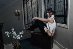 a woman sitting on top of a suitcase next to a vase with flowers in it